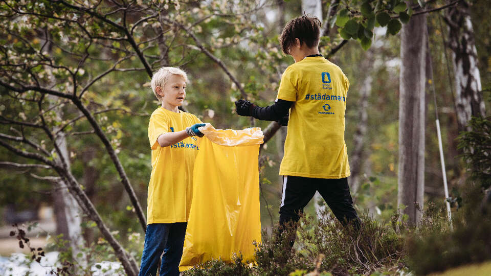 Två pojkar plockar skräp i skogen